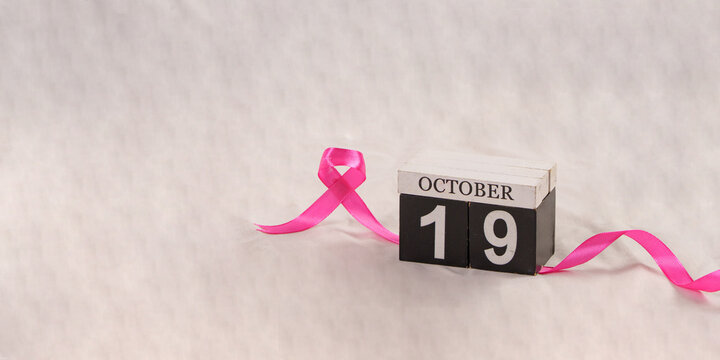 Wooden calendar set to October 19 with pink ribbon for breast cancer awareness day