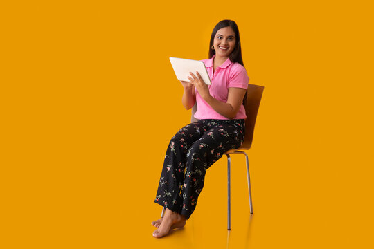 An Indian girl sitting on chair with holding a tablet in her hand 