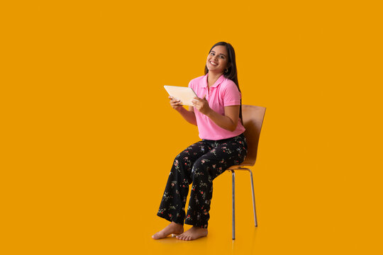 Indian girl posing in front of camera while sitting on chair and holding tablet in her hand