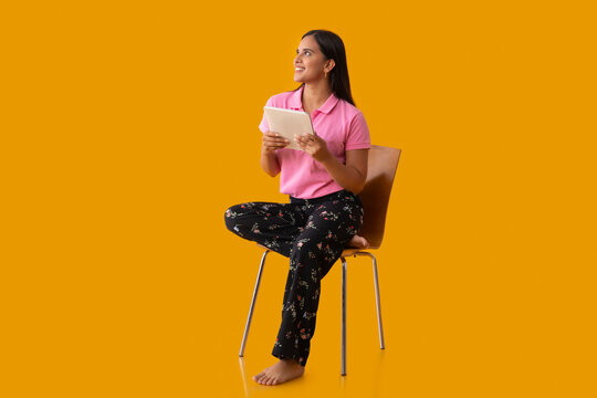 Happy Indian girl looking away while sitting on chair with holding tablet in her hand