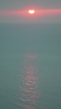 Sunset ocean horizon featuring a bright orange sun sinking into the calm sea with vibrant pink reflections on the water surface