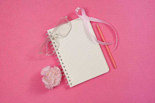 Breast cancer awareness concept with notebook pink ribbon glasses and flower on pink background