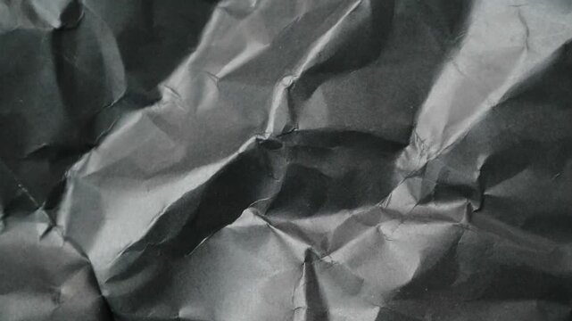 Abstract background of a crumpled sheet of dark grey paper with deep shadows.