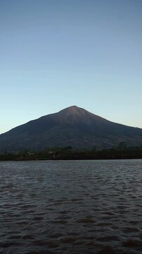 Majestic view of Mount Cikuray in Garut with a calm lake water surface in the afternoon.	