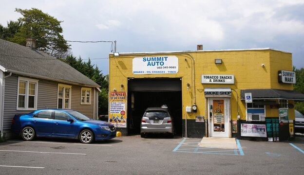 Harrington, Delaware, U.S.A - Aug 1, 2026 - A yellow building housing Summit Auto repair shop and Summit Mart smoke shop with signage and parked vehicles.