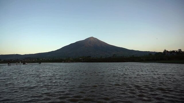 Majestic view of Mount Cikuray in Garut with a calm lake water surface in the afternoon.	