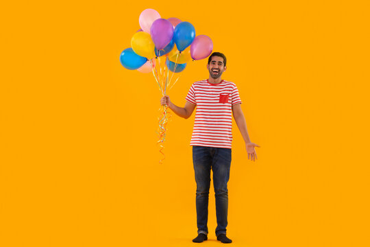 Happy young man standing with bunch of balloons in his hand
