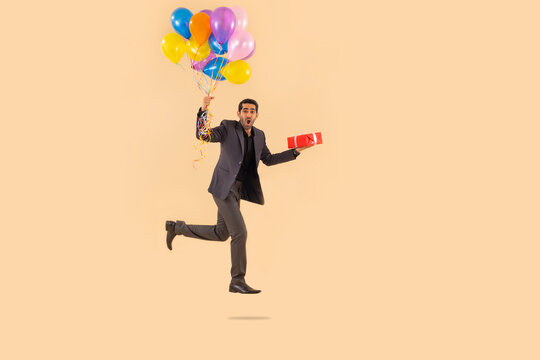 Happy businessman flying with air balloons with gift in hand