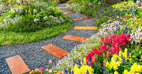 Obraz premium Wooden path in the garden in summer time. Colourful Flowerbeds in a good care maintenance landscapes and walkway