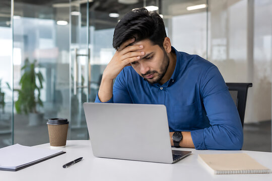 Stressed professional sitting at a laptop with his hand on his forehead, expressing workplace pressure, fatigue, frustration, deadlines, burnout, and mental overload during office work