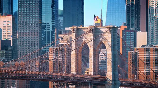 Brooklyn Bridge stone towers against Manhattan buildings. Suspension cables form dense geometric lines across the sunlit urban background.