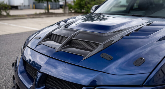 Vented blue performance hood with raised center scoop, mesh openings, and hood fasteners. A detailed workshop view highlights the visible performance upgrade and materials.
