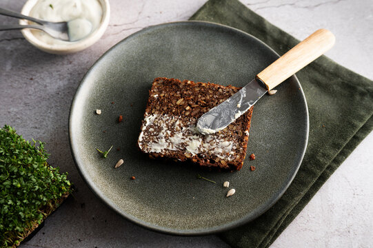 Slice of dark Danish rye bread with spread butter on a plate.