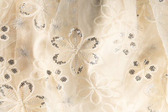 Beige tulle fabric background with floral embroidery, silver sequins, and subtle glitter