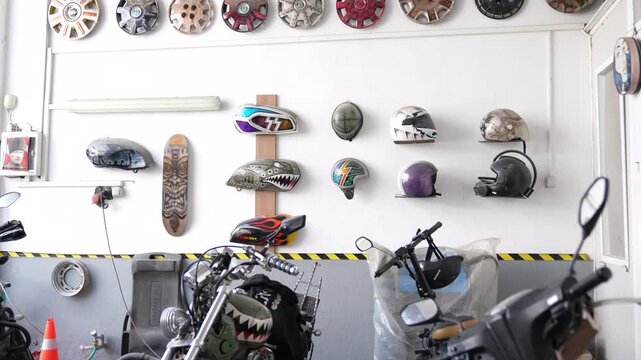 Interior of a custom motorcycle garage with airbrushed helmets, gas tanks, and hubcaps displayed on a white wall. Vintage biker culture and creative workshop concept.