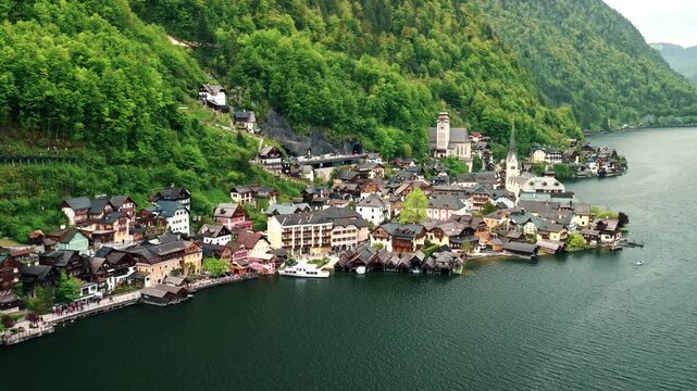 Cinematic aerial drone footage of Hallstatt surrounded by lush green forests, crystal-clear lake, and majestic Alpine mountains.