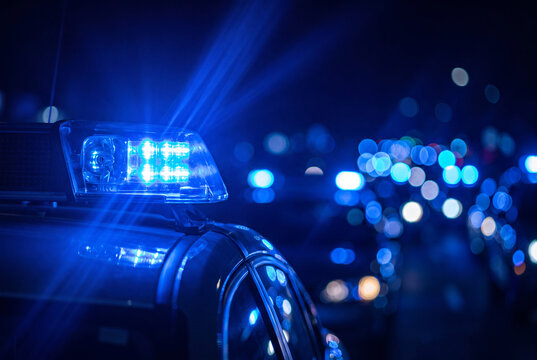 A police emergency blue light flashes intensely at night against a dark background with colorful bokeh city lights.