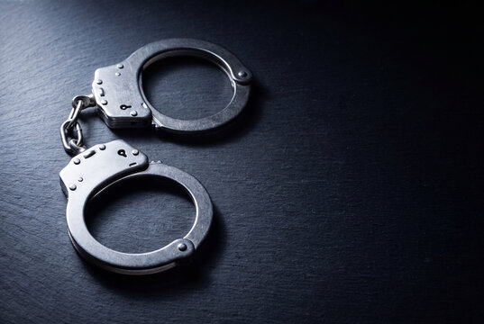 A pair of silver metal handcuffs rests on a dark textured slate surface with generous copy space.
