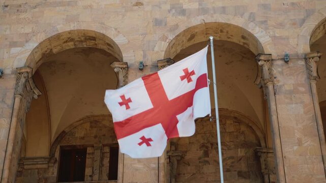 National flag of Georgia waving in front of an arched stone building