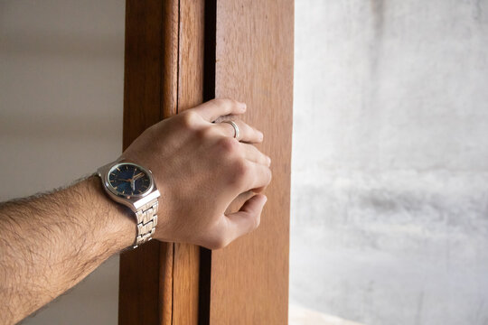 Man wearing a silver wristwatch with a dark dial opening a wooden door