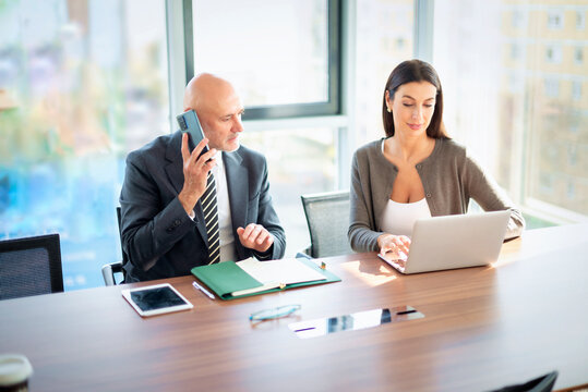 Two mid-aged business people working together on a laptop in a modern office