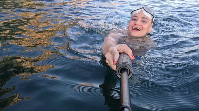 Joyful lady recording her vacation in deep blue lake water. Handheld action camera POV shot.