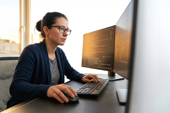 Software developer working on code at dual monitor workstation