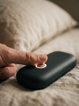 Finger Pressing Glowing Button on Sleek Black Smart Home Sleep Tracker Device