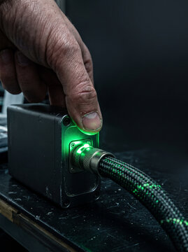 Finger Pressing Green Lighted Power Connector on Industrial Metal Device