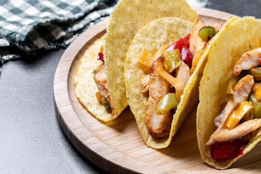 Chicken tacos with bell peppers and onions on black background