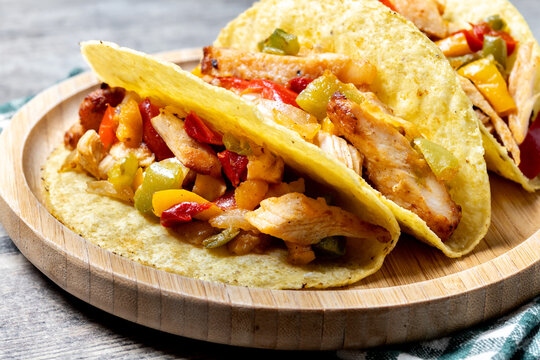 Mexican chicken tacos with bell peppers and onions on wooden table