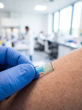 Hand in Blue Glove Applying SweatLab Biosensor Patch to Arm Skin