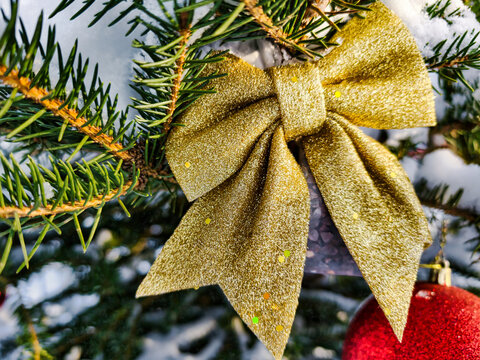 A green Christmas tree stands covered in snow with bright ornaments and a gold bow. The scene captures the festive spirit of the winter holiday season