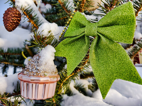 A decorated Christmas tree stands in the snow. The tree features a cupcake ornament and a green bow. It is winter and the scene is festive
