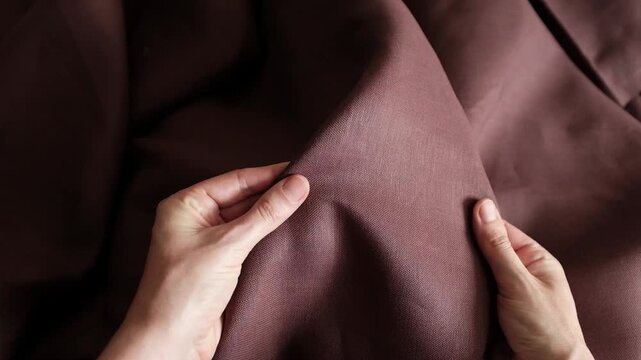 A high-detail, close-up shot moves across draped brown fabric, showcasing its fine weave and soft, elegant folds. For background textures, fashion design presentations, textile industry