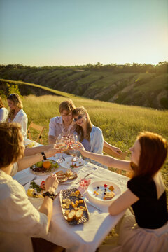 Friends enjoying colorful seasonal dishes at long outdoor table in countryside. Concept of healthy eating, seasonal cuisine, mindful social dining.