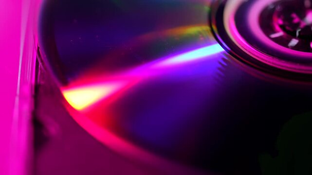 Macro view of a compact disc reflecting vivid pink, blue and green neon light around its central hub. Concept music, data storage, retro technology, advertising and digital design.