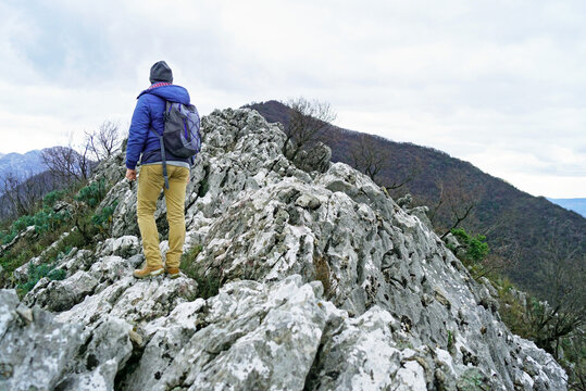 Hiker walks across exposed limestone ridge on Vrmac peninsula in Montenegro. Illustrates off-season mountain travel, solitary hiking beyond peak tourism, and quiet exploration of coastal highlands.
