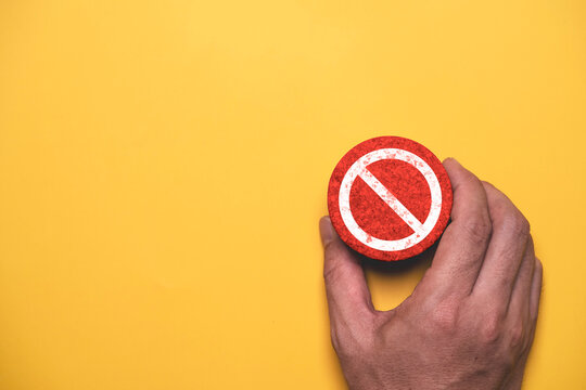 A hand holding a prohibition sign on a yellow background represents stop, restriction, safety rules, workplace compliance, risk prevention, and public warning with ample copy space.
