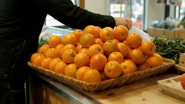 Natural market scene showing ripe juicy oranges piled neatly inside a rustic wicker basket on a store counter illuminated by soft natural daylight to highlight appetizing color in 4K