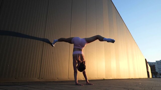 Athletic Woman Performing Handstand Split At Sunset Outdoors