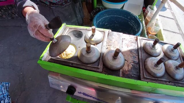 Video of Hand places lid on Indonesian traditional pancake maker. Food vendor prepares grilled pancakes. Bright green appliance sits on street corner. Steam rises gently from cooking units. 4K Footage