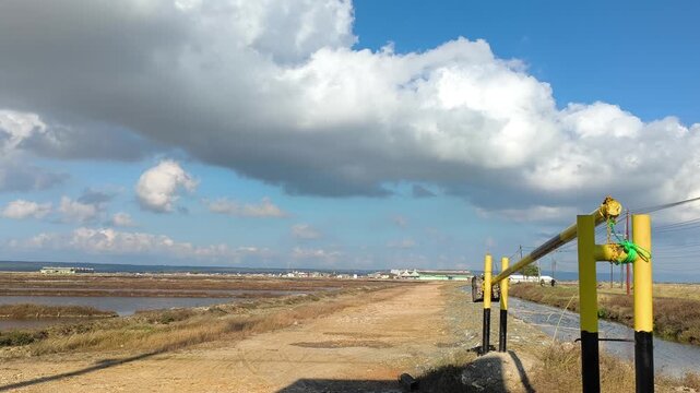 Salt farm landscape with yellow barrier gate under bright blue sky with cumulus cloud