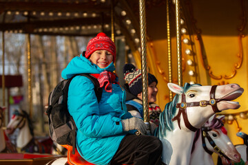 Child enjoys riding a carousel on a sunny day at an outdoor amusement park in winter season © Светлана Лазаренко