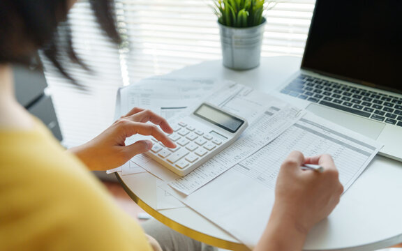 Woman calculating household expenses with a calculator, receipts and laptop for accurate budget planning and personal finance management.