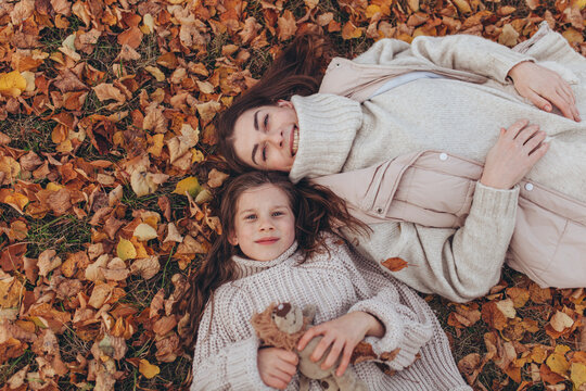 Top view of mother and daughter lying on fallen autumn leaves in park.Tender, heartwarming moment of family connection, love, beauty of autumn season, family lifestyle, parenting and happiness.