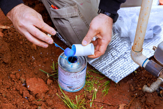 Worker stands in dirt, using adhesive blue glue of plastic pipe with water PVC