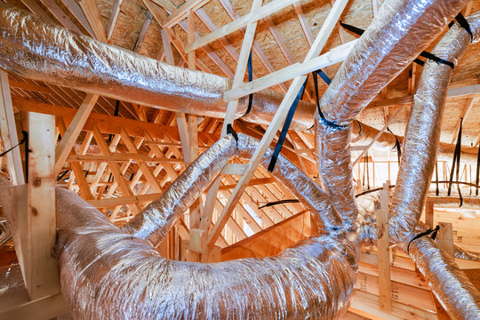 Workers install ductwork in building with wooden framing exposed structures during construction.