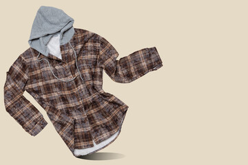 Brown hooded plaid flannel shirt floating in the air with copy space on beige background. Casual fleece lined shacket levitating in store banner concept © aneduard
