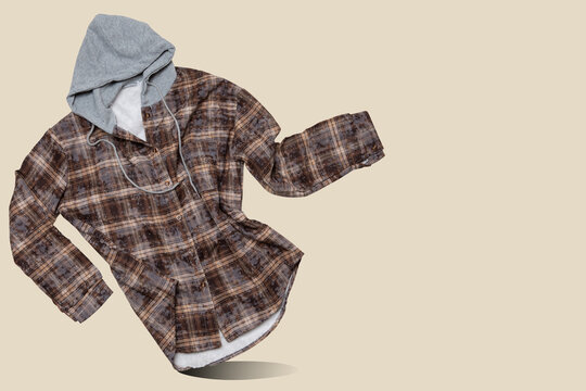Brown hooded plaid flannel shirt floating in the air with copy space on beige background. Casual fleece lined shacket levitating in store banner concept